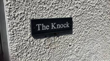 Un letrero negro con letras blancas sobre una pared texturizada, que dice 'The Knock'.