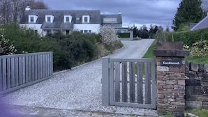 Un camino de grava que conduce a una entrada cerrada con un muro de piedra y un letrero que dice "Knockinreoch".