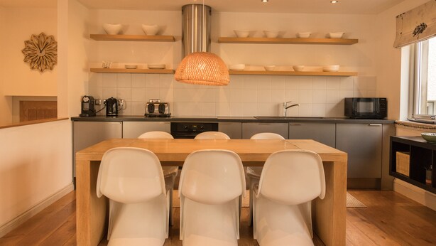 Una cocina moderna con sillas blancas, una mesa de comedor de madera y estanterías empotradas.