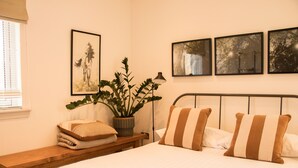 Un dormitorio ordenado con una cama, almohadas, una mesita de noche con una planta y cuadros enmarcados en la pared.