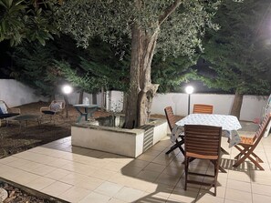 Un patio al aire libre con una mesa y sillas, rodeado de árboles y un piso de baldosas.