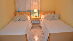 Una habitación doble con dos camas, una mesita de noche con lámpara y una ventana con cortinas.