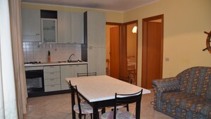 Una cocina compacta con una mesa de comedor y sillas, un sofá, y una puerta de madera que da a otra habitación.