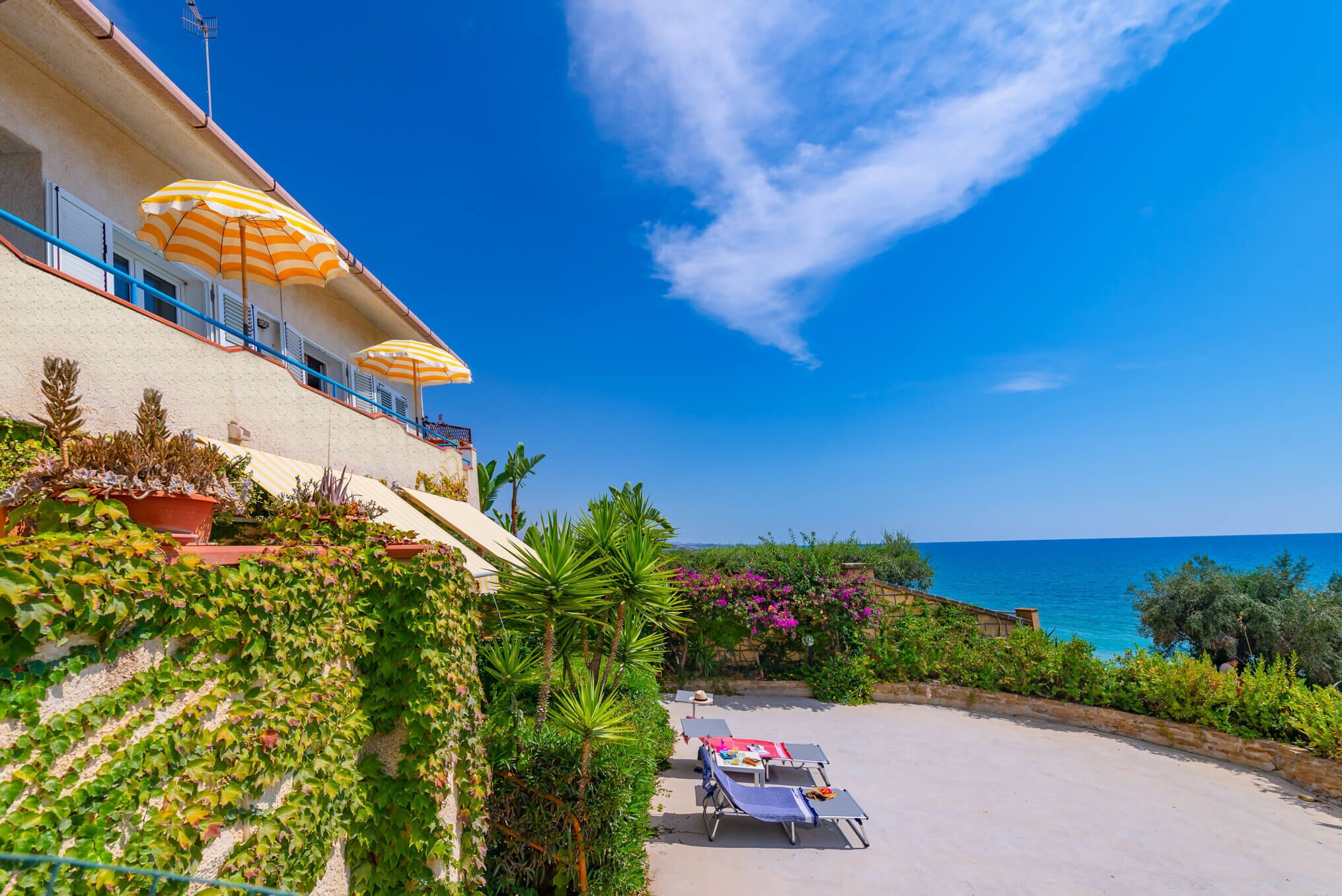 A hotel balcony with outdoor seating and a view of the sea.