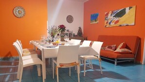 A dining area with a table set for six, surrounded by white chairs, a sofa, and decorative plates on the walls. - Apartment Lumia Big Superior (Sciacca)