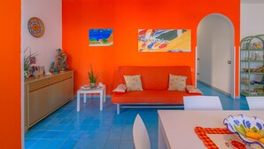 A living room with a bright orange wall, a sofa, and two paintings. - Apartment Lumia Big Superior (Sciacca)