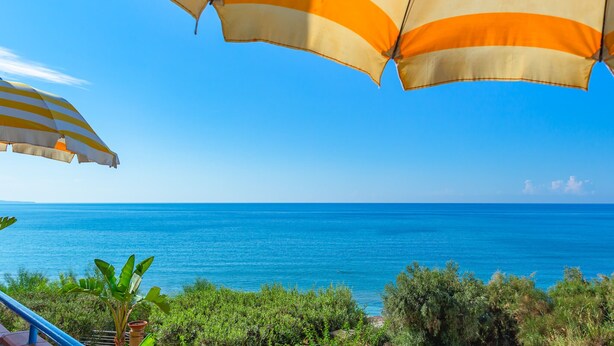 A seaside view with a clear sky, a blue sea, and two striped umbrellas. - Apartment Lumia Big Superior (Sciacca)