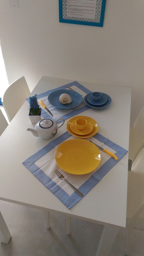 Een eettafel gedekt met gele borden, een witte theepot en een blauwe placemat.