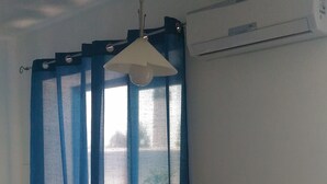 A room with a white chair, a blue curtain, and an air conditioning unit on the wall. - CASA VACANZE A MATTINATA - GARGANO (Mattinata)