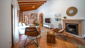 A spacious living room with a fireplace, a television, and a cozy seating area with a wicker chair and a small table. - Cozy estate "It's Bellveret" (Manacor)