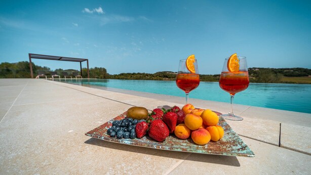 A poolside table with a fruit platter and two glasses of red beverage, overlooking a pool and a clear sky. - Cozy estate "It's Bellveret" (Manacor)