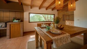 A dining area with a wooden table set for two, a kitchen with a stove, and a window with a view of trees. - Cozy estate "It's Bellveret" (Manacor)