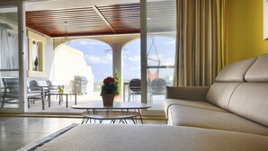A modern living room with a sofa, a round table with a potted plant, and a view of the cityscape through large glass doors. - Three bedroom, luxury apartment with private pool (Ix-Xagħra)