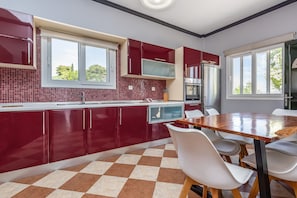 A modern kitchen with red cabinets, a wooden dining table, and a checkered floor. - Private hillside villa with heated pool and magnificent views over Ionian Sea (HR8P+WW Sinarades)