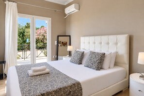 A hotel room with a large bed, a nightstand, a lamp, a window with curtains, and an air conditioning unit.