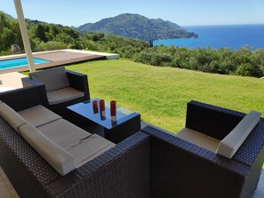 A patio area with wicker furniture, a glass table, and a view of the sea and mountains. - Private hillside villa with heated pool and magnificent views over Ionian Sea (HR8P+WW Sinarades)