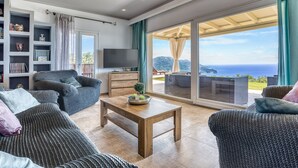 Un salon spacieux doté d’une grande fenêtre donnant sur la mer, d’une table basse en bois, d’un canapé et d’une bibliothèque.