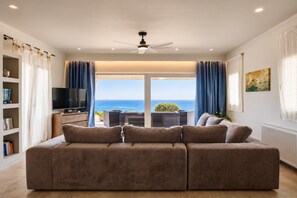 A living room with a sofa, a TV, and a view of the sea.