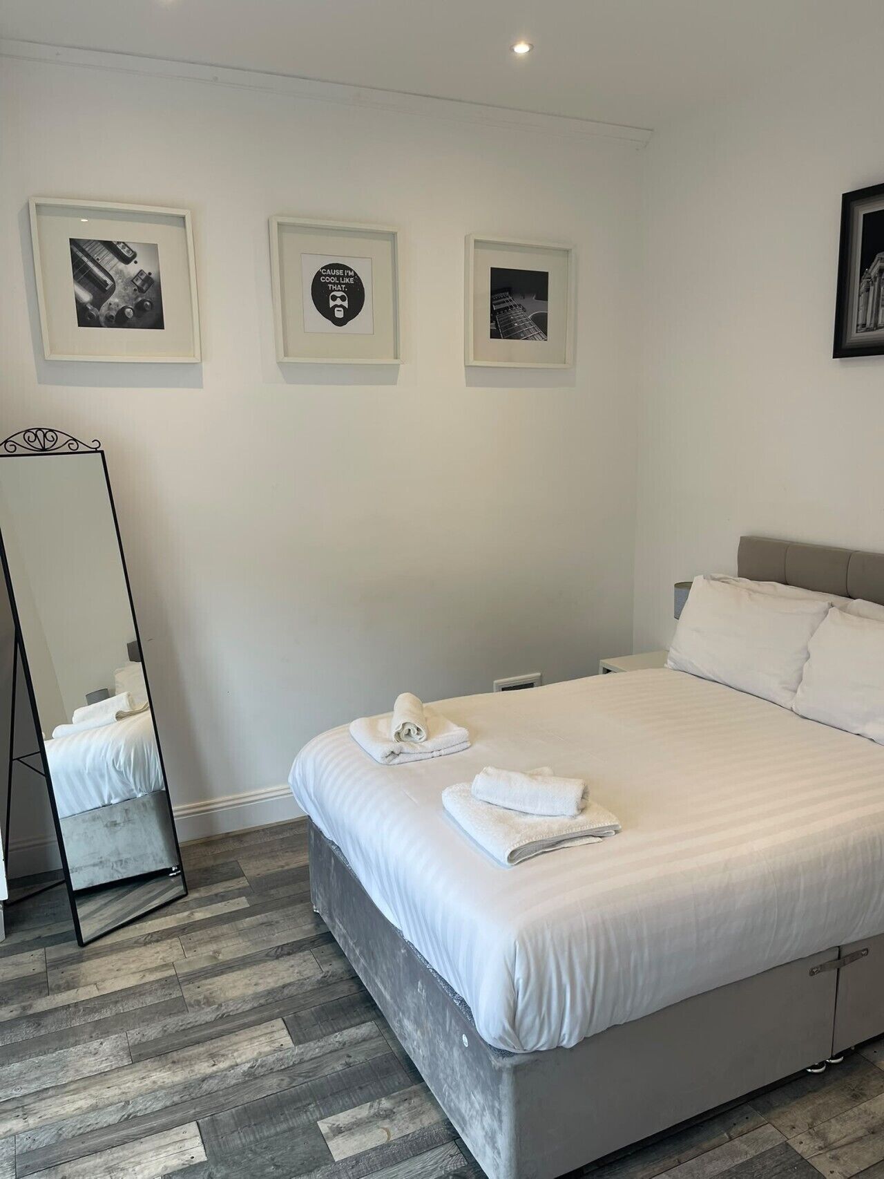 A hotel room with a bed, a mirror, and three framed pictures on the wall.