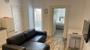 Una sala moderna con un sofá de cuero negro, un mueble bajo para televisor blanco y suelo de parquet de madera.