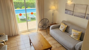 A living room with a grey sofa, two cushions, a wooden coffee table, a floor fan, and a view of a pool through a glass door. - Villa Cristina, air conditioning, private pool, free WiFi (Binibeca)