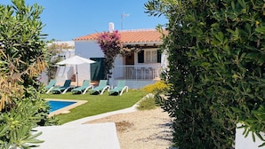 A poolside area with lounge chairs, a white umbrella, and a building with a red-tiled roof. - Villa Cristina, air conditioning, private pool, free WiFi (Binibeca)