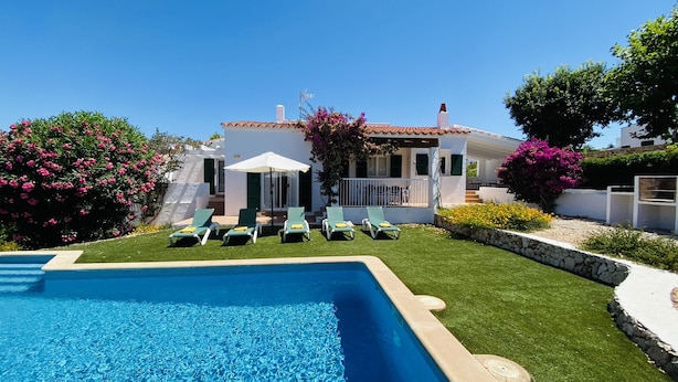 A poolside area with a clear blue pool, a white building with a tiled roof, and a well-maintained lawn. - Villa Cristina, air conditioning, private pool, free WiFi (Binibeca)
