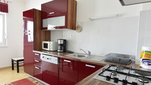 Pieni, käytännöllinen keittiö, jossa on punaiset kaapit, mikroaaltouuni, kahvinkeitin, kaasuliesi ja pesuallas.