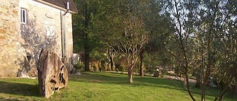 Ein Steinhaus mit geneigtem Dach, ein großer Baum im Vorgarten und ein klarer Himmel.