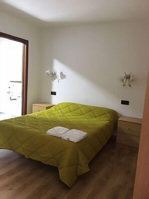 Une chambre à coucher avec une couvre-lit verte, deux oreillers, une commode en bois et une table de chevet.