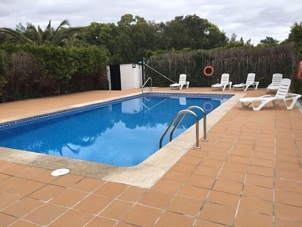 Une piscine rectangulaire dont le bord est recouvert de carreaux, entourée d’une terrasse également carrelée. Plusieurs chaises longues blanches sont alignées le long du bord de la piscine.