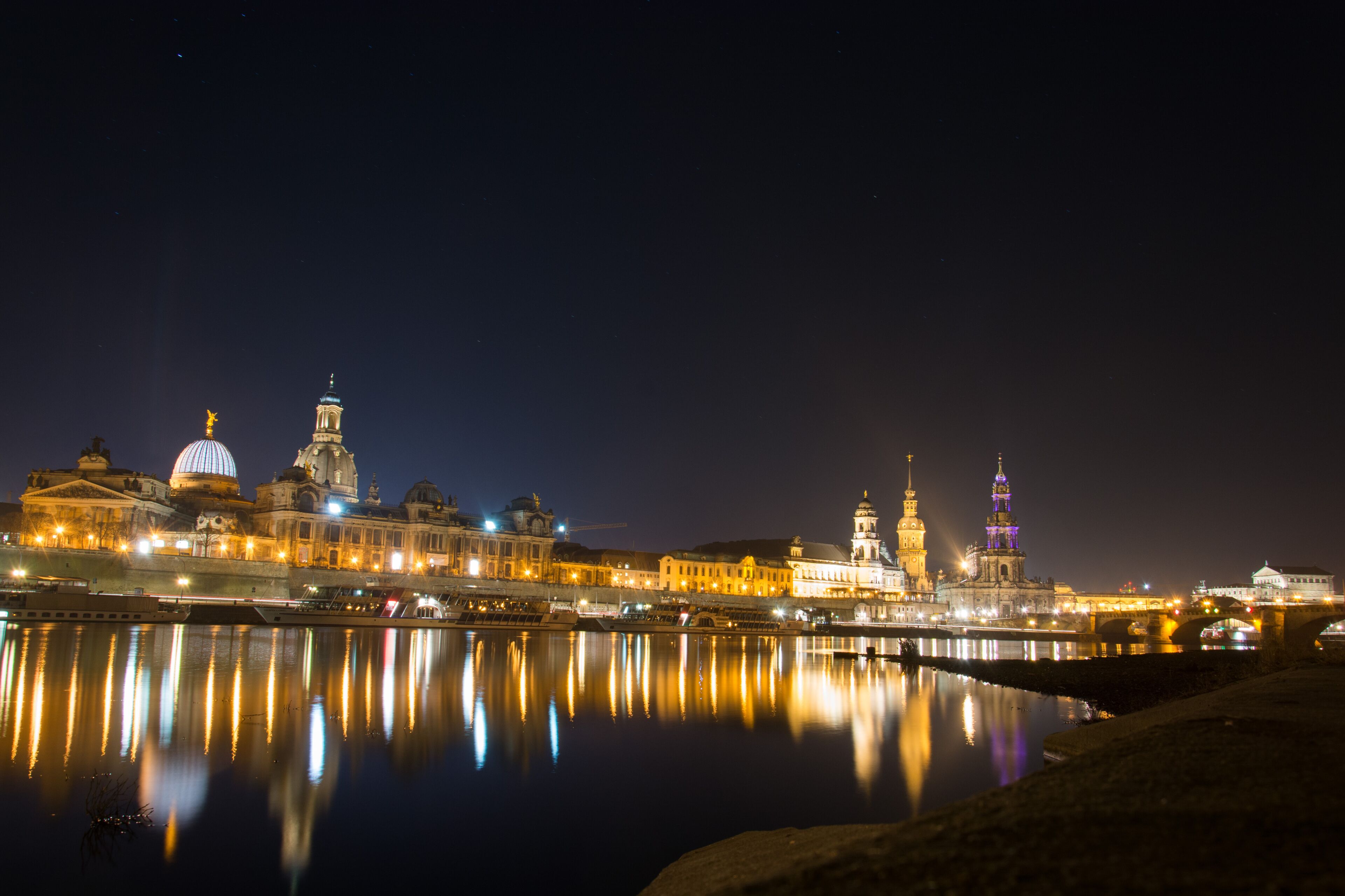 A nighttime cityscape with illuminated buildings reflecting on the water.