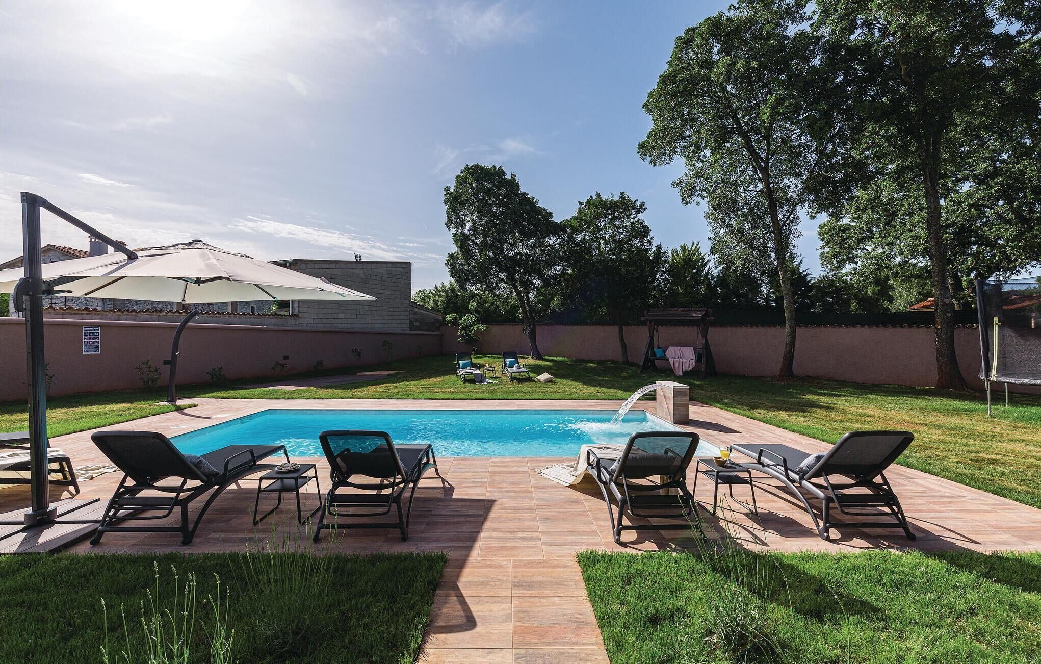 A backyard with a swimming pool, lounge chairs, and a pergola with a patio umbrella.