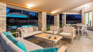 An outdoor patio area with a sofa, chairs, and a table. There is a pool visible in the background. - Amazing home in Sajini (Sajini)