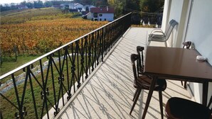 En balkong med ett bord och stolar, med utsikt över en vingård och hus.