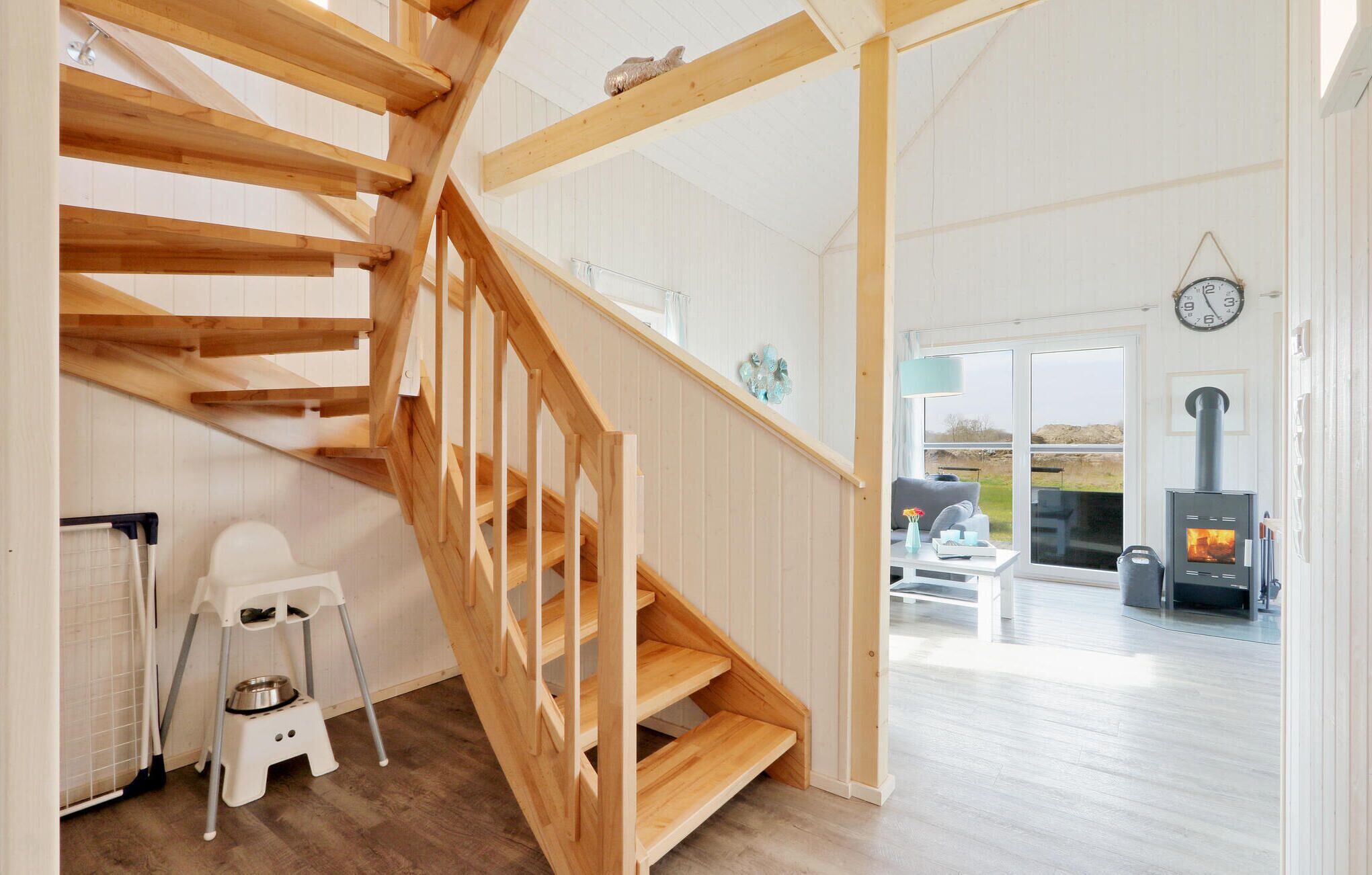 A wooden staircase leading to a living area with a fireplace, a pet feeding station, and a view of the outdoors.