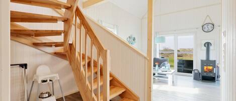 A wooden staircase leading to a living area with a fireplace, a pet feeding station, and a view of the outdoors.