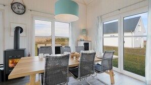 A dining area with a wooden table, wicker chairs, a black stove, and a view of the outdoors. - Awesome home in OstseeResort Olpenitz with sauna (OstseeResort Olpenitz)