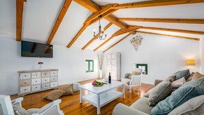 Un salon spacieux avec des poutres apparentes, une table basse blanche, un téléviseur et un coin salon confortable.