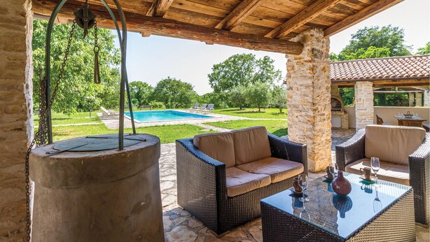 Un espace extérieur aménagé en terrasse, avec des meubles en osier, une table en verre et une vue sur une piscine et un jardin.