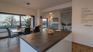 Una cucina moderna con isola centrale, zona pranzo con sedie e tavolo, e vista sull'esterno.
