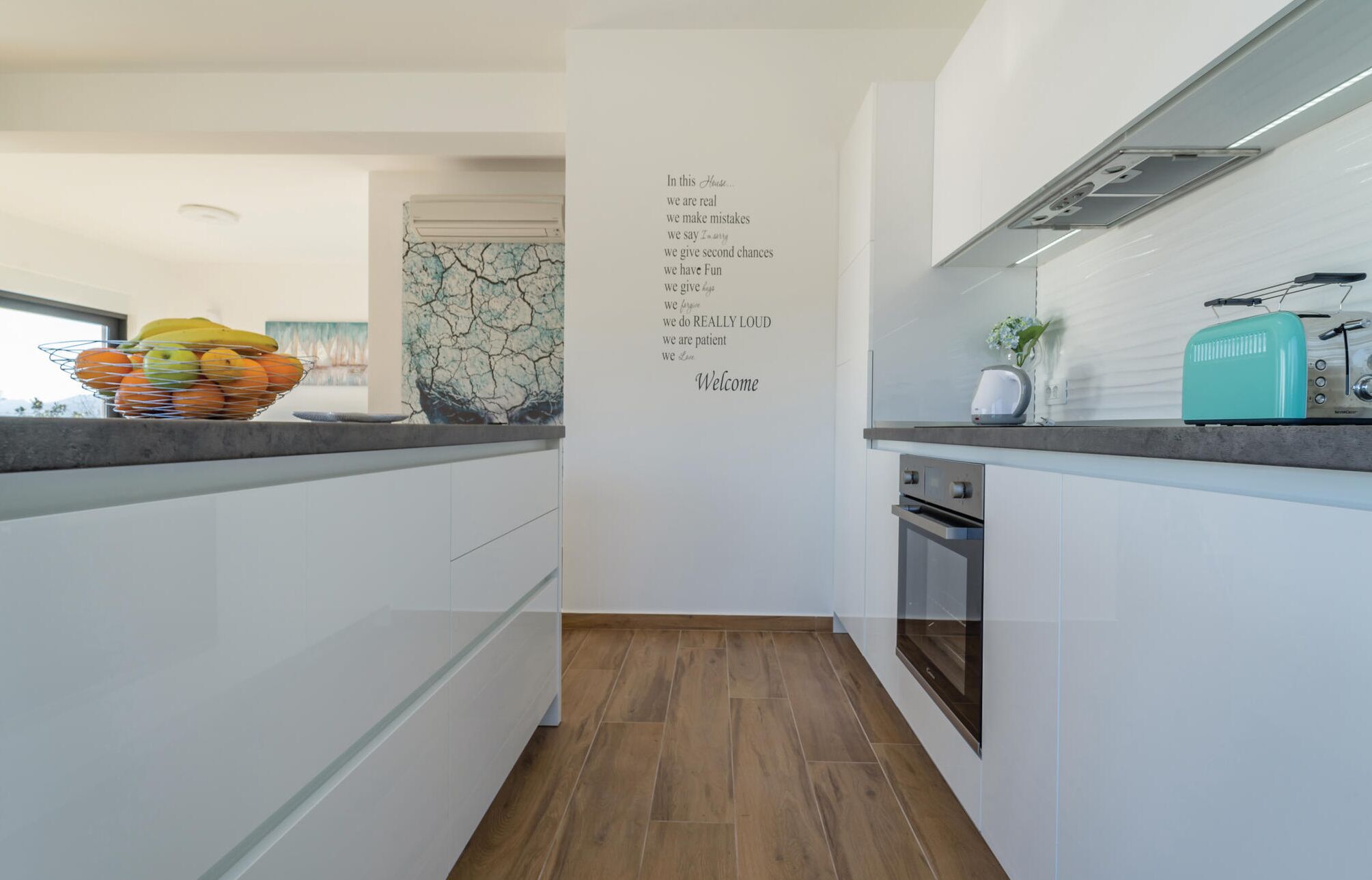 A modern kitchen with white cabinets, a wooden floor, and a wall with motivational quotes.