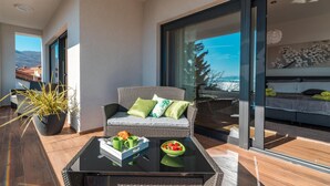 Un balcone con un divano in vimini, un tavolino in vetro e prodotti per la colazione, con vista sulla città e sulle montagne.