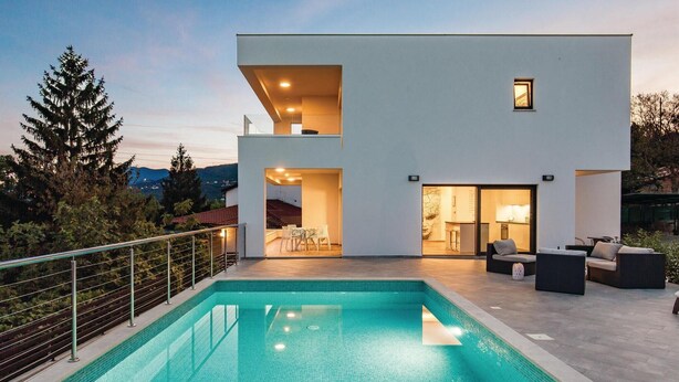 Una moderna casa a due piani con piscina, area salotto esterna e vista sul paesaggio circostante.