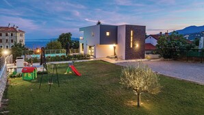 Una casa moderna con un prato curato, un'area giochi per bambini e vista sul mare.