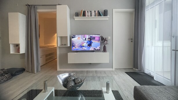 En moderne stue med et fladskærms-TV, et glasbord, en sofa og en bogreol.