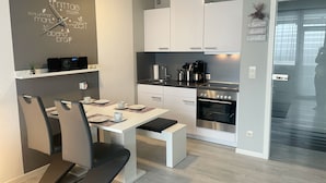 Et moderne køkken med hvide skabe, indbygget ovn og kaffemaskine.