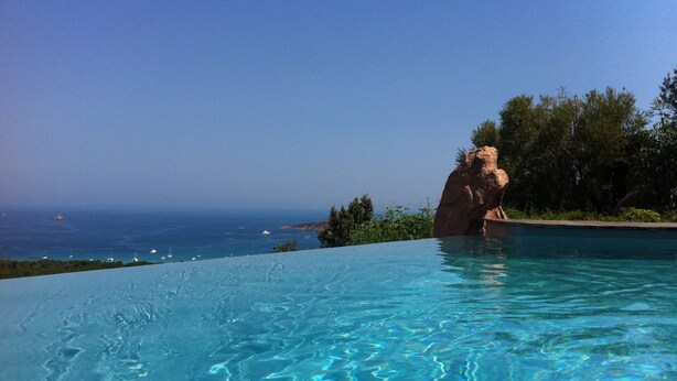 An infinity pool with clear blue water, a large rock formation, and a view of the ocean. - EXCEPTIONAL VIEW PINARELLO BAY AND NEEDLES BAVELLA Private Pool (Zonza)