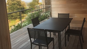 A wooden deck with a table and chairs, overlooking a garden and distant trees. - EXCEPTIONAL VIEW PINARELLO BAY AND NEEDLES BAVELLA Private Pool (Zonza)