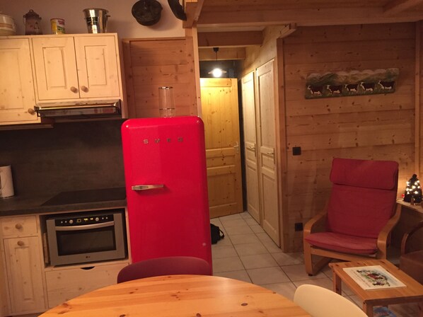 A compact kitchen with a red refrigerator, wooden cabinets, and a dining area with a table and chairs. - APARTMENT MANIGOD - The ÉTALE (La Clusaz) to SKI FOOT (MANIGOD)